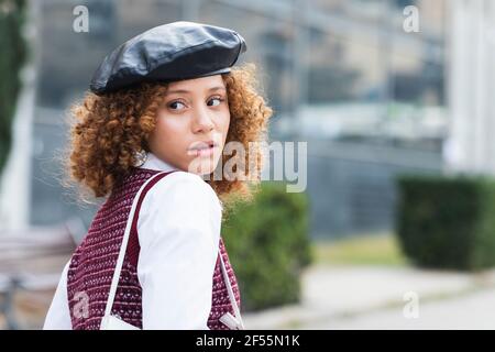 Lockiges Haar Teenager-Mädchen trägt Baskenmütze Blick über die Schulter, während Im Freien stehen Stockfoto