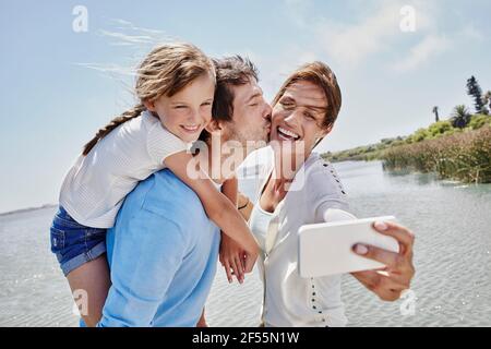 Fröhliche Familie, die Selfie über das Mobiltelefon am See gemacht hat Stockfoto