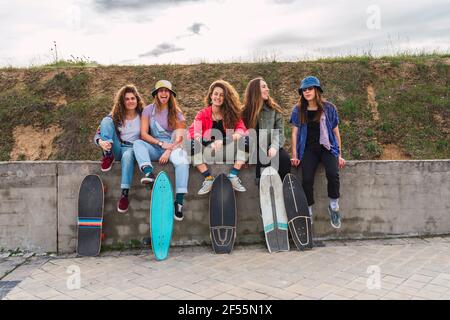 Fröhliche Freundinnen mit Skateboards, die auf einer Stützwand sitzen Stockfoto