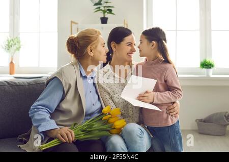 Das kleine Mädchen gratuliert ihrer Mutter und Großmutter zum Urlaub, indem es ihnen Geschenke gibt. Stockfoto