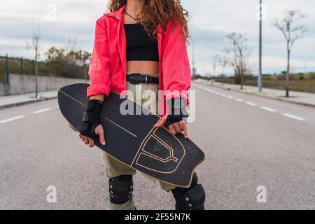 Frau trägt fingerlose Handschuhe, während sie das Skateboard auf der Straße hält Stockfoto