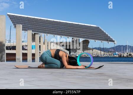 Sportlerin, die Kinder trainiert, posiert mit dem Yoga-Rad an der Promenade Sonniger Tag Stockfoto