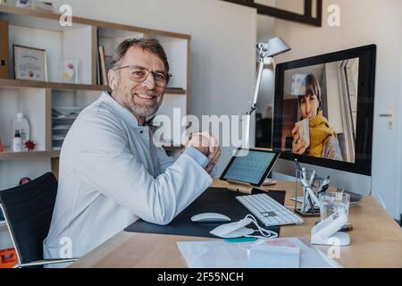 Lächelnder Arzt mit Patient über Videoanruf am Computer bei Arztpraxis Stockfoto