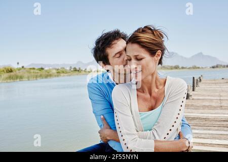 Reifer Mann küsst sich, während er Frau auf dem Pier umarmt Stockfoto