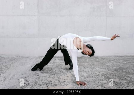 Flexibler Mann, der sich nach hinten beugt, während er gegen die weiße Wand tanzt Stockfoto