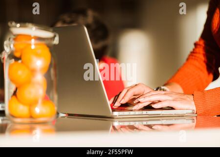 Frau mit Laptop, die zu Hause von einem Sohn beim Essen arbeitet Tabelle Stockfoto
