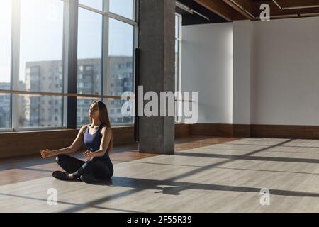 Lifestyle, Wohlbefinden und Sportkonzept. Frau, die auf dem Boden des Fitnessraums sitzt und aktiv Sport-BH Leggings trägt, meditiert, Yoga-Übungen praktiziert Stockfoto