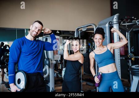 Lächelnde Sportler, die Muskeln spielen lassen, während sie im Fitnessclub stehen Stockfoto