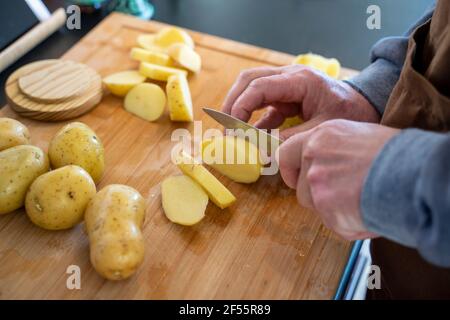 Älterer Mann, der in der Küche Rohkartoffeln auf Schneidebrett schneidet Stockfoto