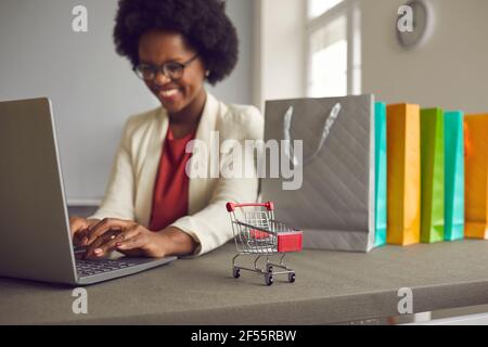 Spielzeugwagen auf einem Tisch in der Nähe von Einkaufstaschen und neben einer Frau, die online einkaufen. Stockfoto