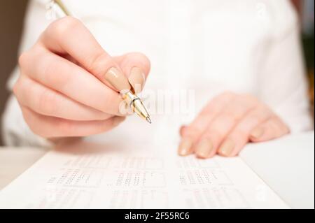 Weibliche Hand hält einen Stift, um das Datum im Kalender zu markieren. Kalendererinnerung, tägliche Planung Stockfoto