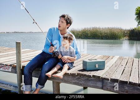 Reifer Mann und Junge fischen zusammen, während sie auf dem Pier sitzen Stockfoto