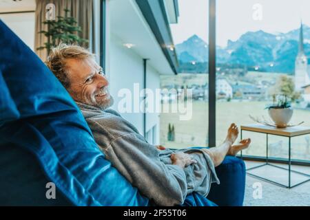 Lächelnder Mann, der sich auf einem Schaukelstuhl vor dem Fenster entspannt Im Hotelzimmer Stockfoto