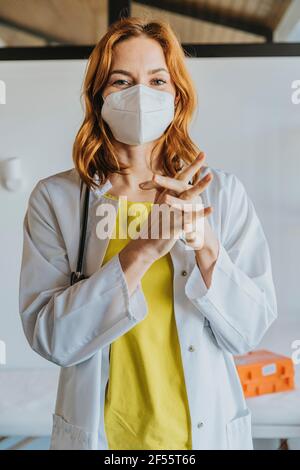 Weibliche Mitte Erwachsene Arzt trägt Gesichtsmaske Desinfektion Hände mit Desinfektionsmittel, während Sie in der Klinik stehen Stockfoto