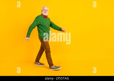 In voller Länge Foto von lustigen süßen reifen Mann gekleidet Pullover Fliege Gläser gehen leeren Raum isoliert gelbe Farbe Hintergrund Stockfoto