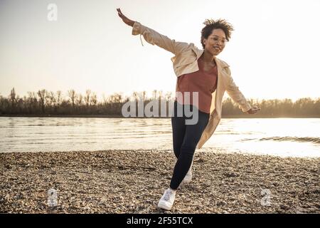 Glückliche Frau mit ausgestreckten Armen am See Stockfoto