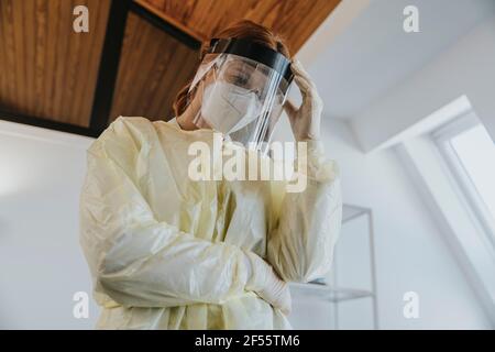 Ärztin mit schützender Arbeitskleidung, die mit der Hand in der Hand steht Im Untersuchungsraum Stockfoto