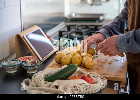 Senior Mann hackt Kartoffeln auf Schneidebrett in der Küche Stockfoto