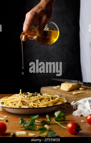 Mann fügte Kapern auf Spaghetti an einem Holztisch hinzu Stockfoto