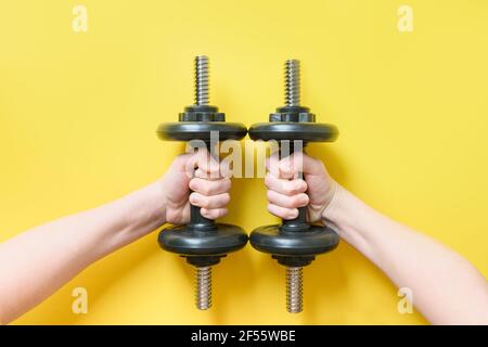 Schwarze Hanteln in Händen auf gelbem Hintergrund. Sportgeräte. Nahaufnahme. Blick von oben. Stockfoto