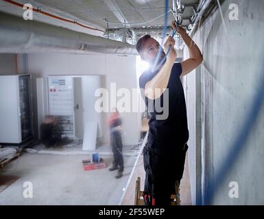 Ein Elektriker installiert Kabel an der Decke in, während er in arbeitet Workshop Stockfoto