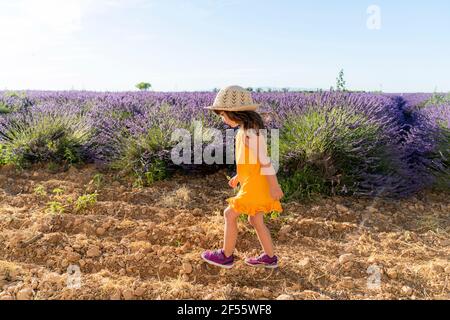 Kleines Mädchen trägt Strohhut zu Fuß in Lavendelfeld während Sommer Stockfoto