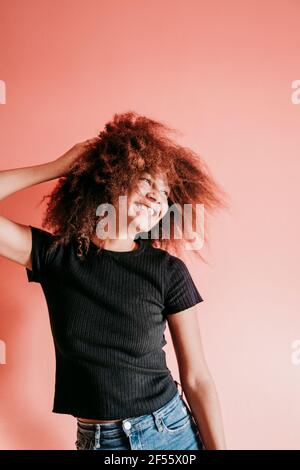 Fröhliche Afro-Frau mit der Hand im Haar, auf die sie absieht Pfirsich Hintergrund Stockfoto