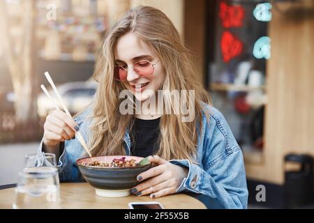 Gut aussehende beliebte Lifestyle-Blogger Blick auf Schüssel mit asiatischem Essen, Bestellung Ramen zum ersten Mal, sammeln Mut zu würzigen Mahlzeit versuchen, halten Stockfoto