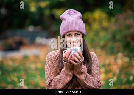 Portrait einer schönen Frau mit rosa Strickmütze im Freien Mit Becher in den Händen Stockfoto