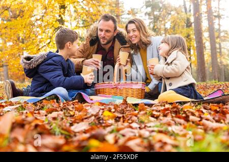 Lächelnde Familie, die zusammen Kaffee trinken, während sie im Wald sitzt Stockfoto