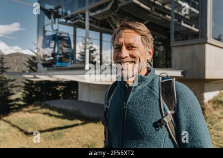 Lächelnder reifer Mann, der an der Bergbahnstation Maria Alm, Salzburger Land, Österreich, steht Stockfoto