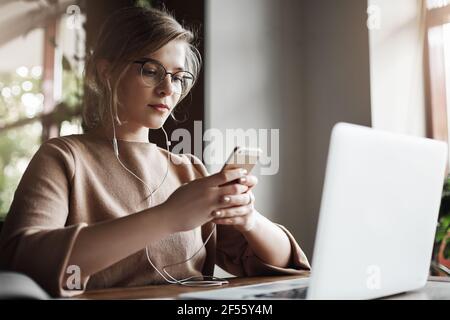 Musik auswählen, um Fokus und Arbeit zu steigern. Porträt von charmanten europäischen Edelstein in Brille mit trendigen Frisur, sitzt in der Nähe von Laptop, tragen Kopfhörer Stockfoto