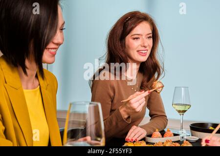 Lächelnde junge Frau mit Sushi, während sie mit Freundinnen sitzt Am Tisch im Restaurant Stockfoto