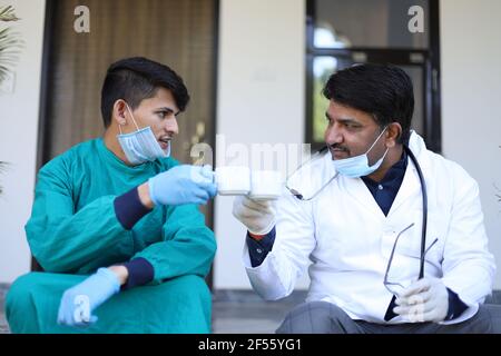 Nahaufnahme von zwei indischen Ärzten mit medizinischer Uniform und Maske trinkt eine Tasse Kaffee Stockfoto