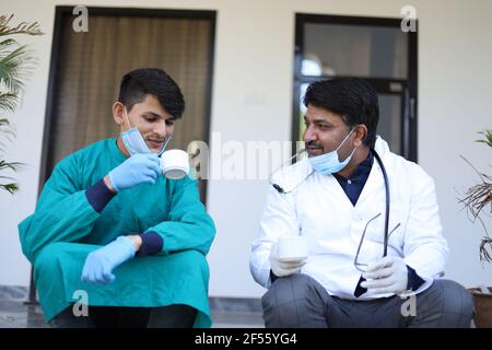 Nahaufnahme von zwei indischen Ärzten mit medizinischer Uniform und Maske trinkt eine Tasse Kaffee Stockfoto