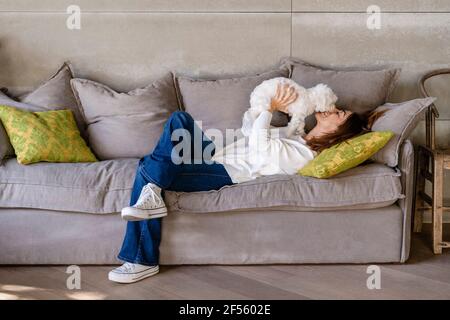 Frau, die mit ihrem Hund spielt, während sie auf dem Sofa liegt Stockfoto