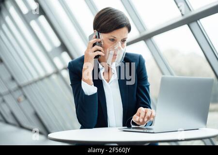 Reife Geschäftsfrau, die im Büro auf dem Smartphone spricht Während der COVID-19 Stockfoto