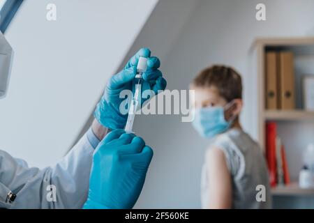 Arzt, der COVID-19-Impfstoff in eine Spritze für Patienten im Hintergrund einfüllt In der Klinik Stockfoto