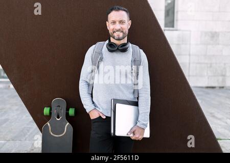 Lächelnder männlicher Unternehmer mit der Hand in der Tasche, die gegen die Wand steht Stockfoto