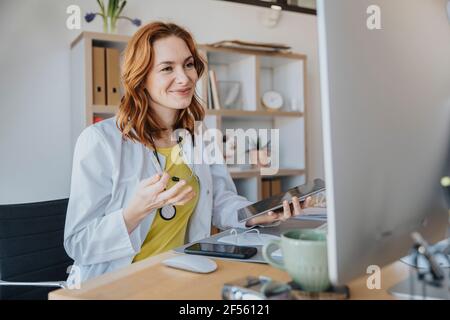 Ärztin mit digitalem Tablet lächelt, während sie mit Video spricht Rufen Sie über den Computer in der Arztpraxis an Stockfoto