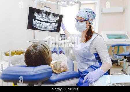 Weibliche Zahnärztin, die einem kleinen Mädchen, das in Zahnärzten liegt, Röntgenaufnahmen zeigt Stuhl Stockfoto