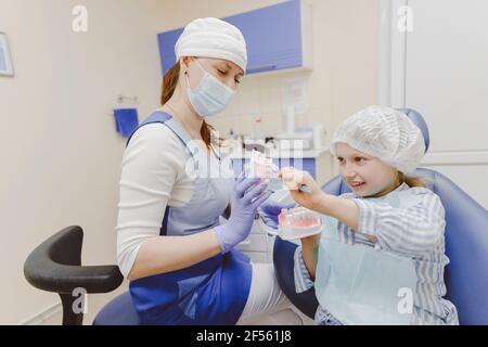 Weibliche Zahnärztin, die dem kleinen Mädchen, das in Zahnärzten sitzt, Prothesen zeigt Stuhl Stockfoto