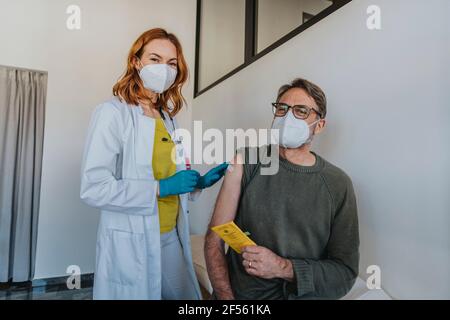 Arzt trägt eine schützende Gesichtsmaske und legt einen Verband, während er neben sich steht Männlicher Patient im Untersuchungsraum Stockfoto