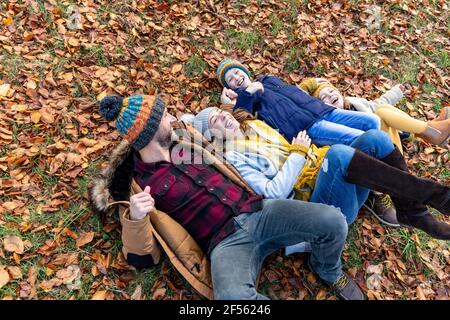Glückliche Familie beim Spielen, während sie im Wald auf Blättern liegt Stockfoto