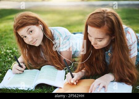 Sie wollten etwas fragen. Portrait of Charming sorglos Rotschopf Mädchen auf Gras im Park mit Stister liegen, teilen Kopfhörer, während Musik hören Stockfoto
