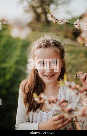 Schwester küsst lächelnden Bruder, während sie unter Mandelbaumbästen sitzt Stockfoto