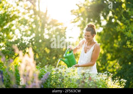 Junge Frau, die Blumen im Garten im Frühling gießt Stockfoto