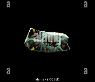 Fragment eines Gefäßes. Eine niedrige Krümmung des Glassfragmentes ermöglicht die Zuordnung zu einem Gefäß, möglicherweise einer Schale. Der mintgrüne Scherbe zeigt mehrere Blüten in millefiori-Technologie. Ein gelber Kreis ist von mehreren roten Kreisen mit schwarzer Kontur umgeben. Die Darstellungen sind leicht verzerrt. Für die Herstellung wurden verschiedenfarbige Gläser zu Rohren und Stäben geformt. Diese wurden komprimiert und erhitzt, was zu einem langen Balken führte. Die Glasscheiben hatten verschiedene amorphe oder florale Muster. ​​now Danach wurden mehrere dieser Thrombozyten gefaltet, wieder erhitzt und in eine Gefäßform gepresst. Grat Stockfoto