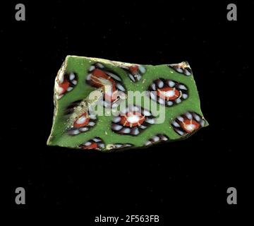 Fragment eines Gefäßes. Eine niedrige Krümmung des Glassfragmentes ermöglicht die Zuordnung zu einem Gefäß, möglicherweise einer Schale. Der grüne Scherbe zeigt mehrere Blüten in millefiori-Technologie. Um einen weißen Punkt mit roter Kontur wird ein violettes Band mit weißen Punkten als Blütenblätter platziert. Für die Herstellung wurden verschiedenfarbige Gläser zu Rohren und Stäben geformt. Diese wurden komprimiert und erhitzt, was zu einem langen Balken führte. Die Glasscheiben hatten verschiedene amorphe oder florale Muster. ​​now Danach wurden mehrere dieser Thrombozyten gefaltet, wieder erhitzt und in eine Gefäßform gepresst. Burry für die aufwendige Manufaktur Stockfoto