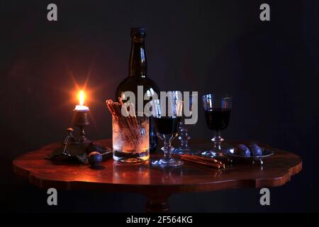 Studioaufnahme einer Flasche Rotwein, drei gefüllte Weingläser, Pflaumen, salzige Brezeln und brennende Kerze auf einem kleinen Couchtisch Stockfoto